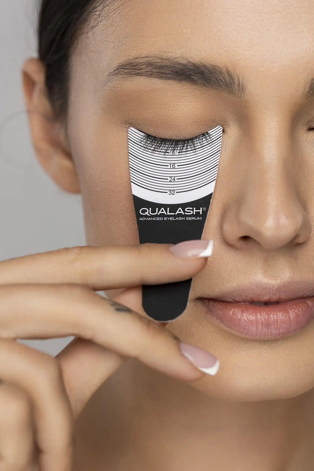 QUALASH® Advanced Eyelash Serum – dark-haired woman measuring lash growth with curved gauge tool